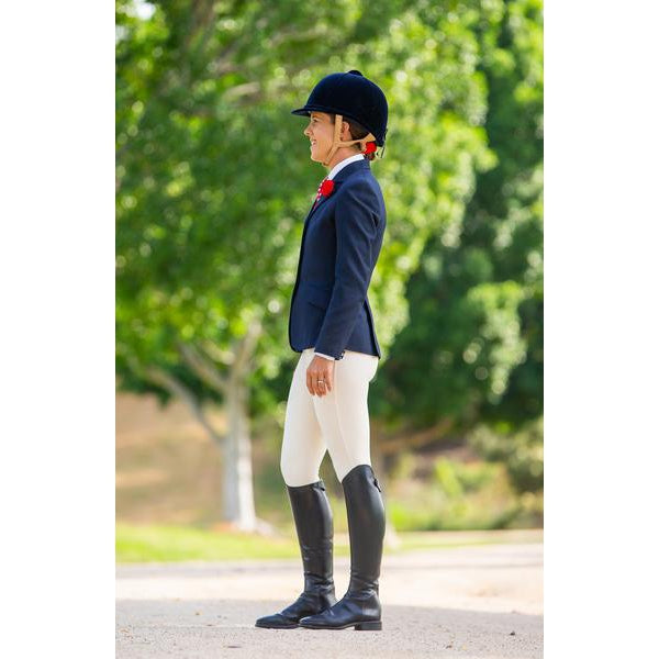 Rider in horse riding tights, jacket, and boots, smiling outdoors.