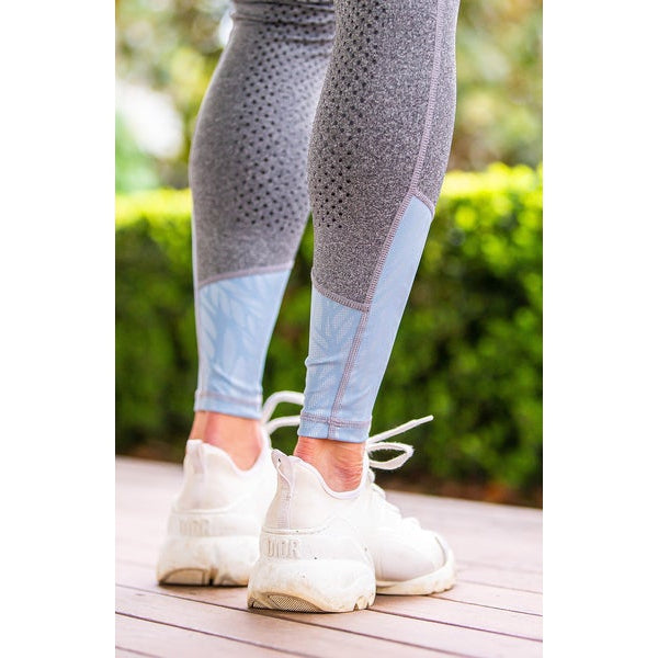 Person wearing grey and blue horse riding tights with white sneakers.