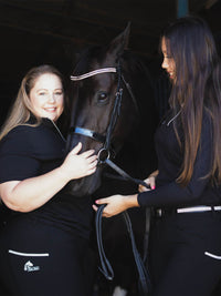 2 women wearing plum tack black riding tops, patting horse