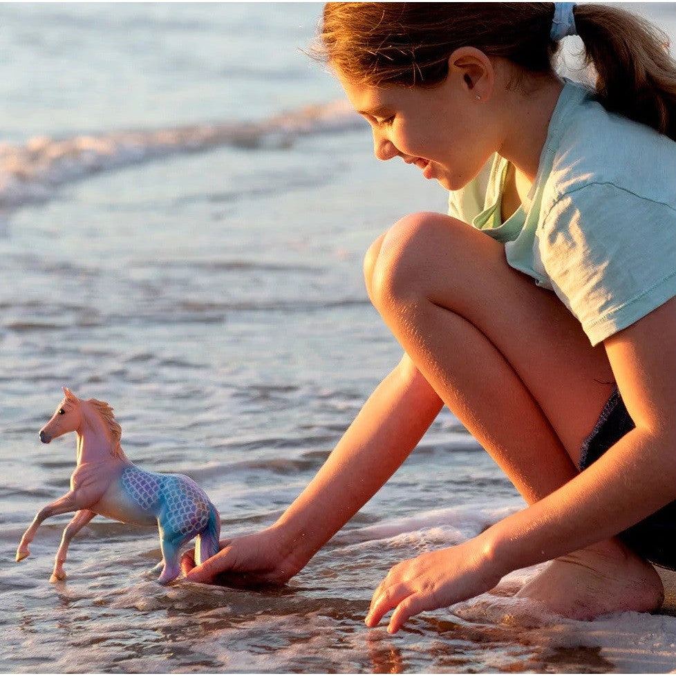 Girl playing with Breyer Horse Toy on the beach at sunset.