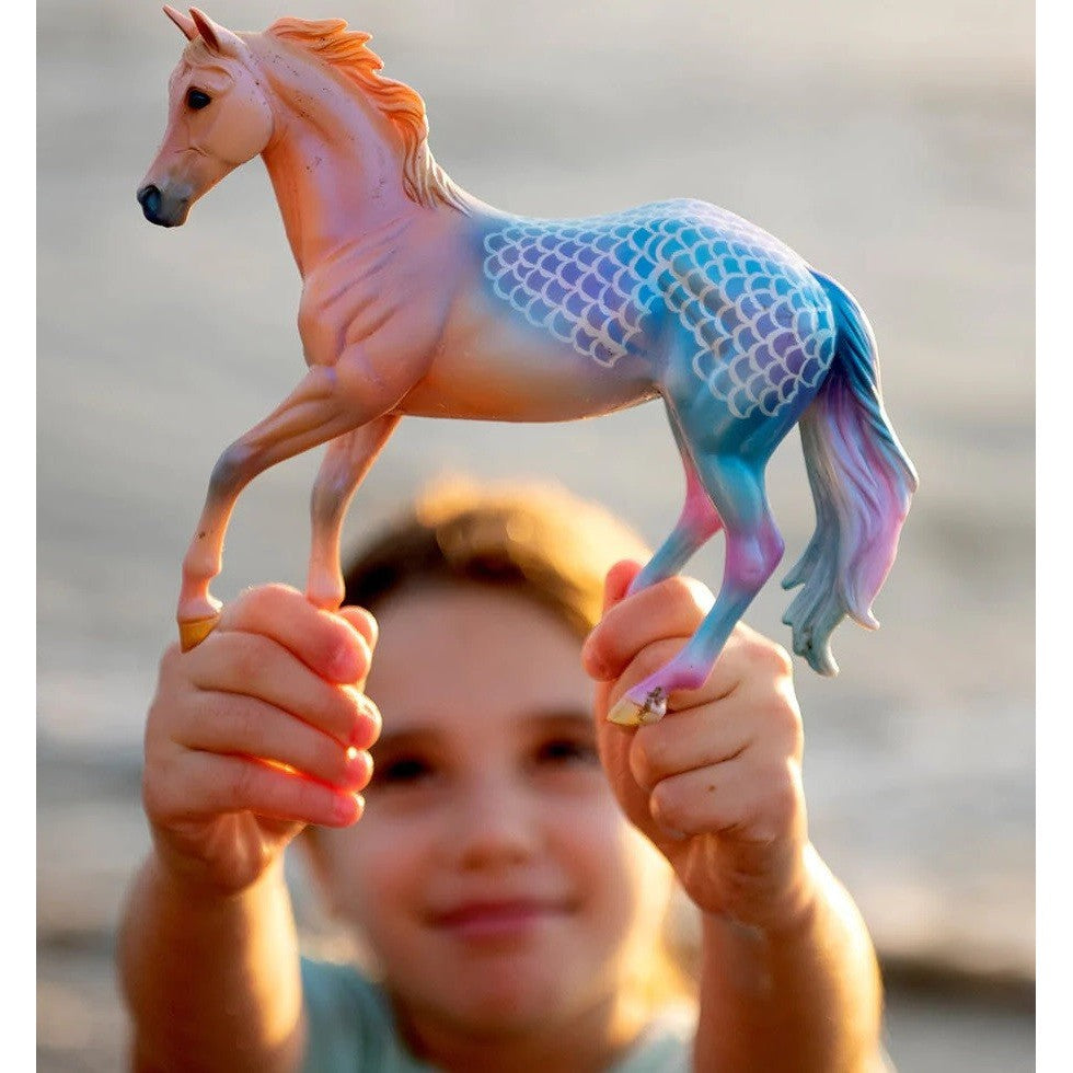 Child holding Breyer Horse Toy with intricate colors at sunset.