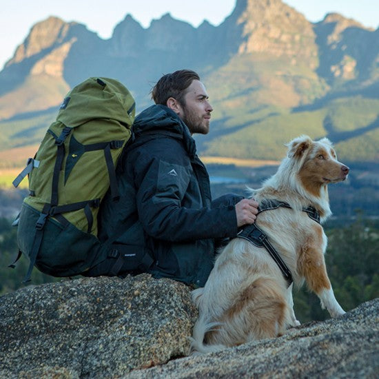 Hiker with backpack and dog wearing Rogz harness outdoors.